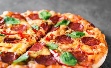 Mozzarella peynirli Pepperoni Pizza, salam, biber, baharat ve taze ıspanak. Koyu gri arka planda İtalyan pizzası