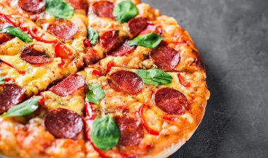 Mozzarella peynirli Pepperoni Pizza, salam, biber, baharat ve taze ıspanak. Koyu gri arka planda İtalyan pizzası