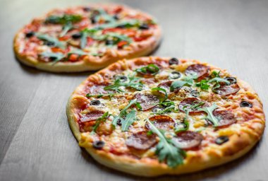 Mozzarella peyniri, Domates, biber, zeytin, Baharat ve Taze arugula ile Pepperoni Pizza ve Pizza. Ahşap masa arka planda Pizza Margherita veya Margarita