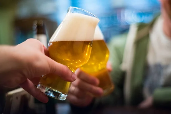 Close-up view of a two glass of beer in hand. Beer glasses clinking in bar or pub