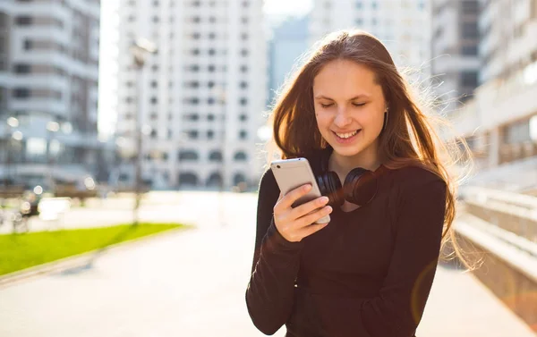 長い髪を持つ若いティーンエイジャーブルネットの女の子の屋外の肖像画 晴れた日に通りでスマートフォンを見て黒いドレスの街の女の子 — ストック写真