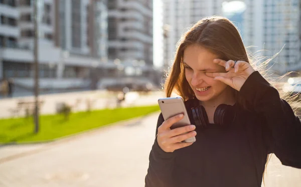 長い髪を持つ若いティーンエイジャーブルネットの女の子の屋外の肖像画 晴れた日に通りでスマートフォンを見て黒いドレスの街の女の子 — ストック写真