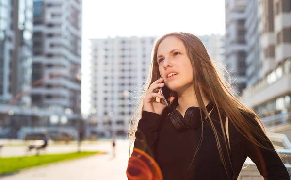 長い髪を持つ若いティーンエイジャーブルネットの女の子の屋外の肖像画 晴れた日に通りでスマートフォンで話す黒いドレスの街の女の子 — ストック写真