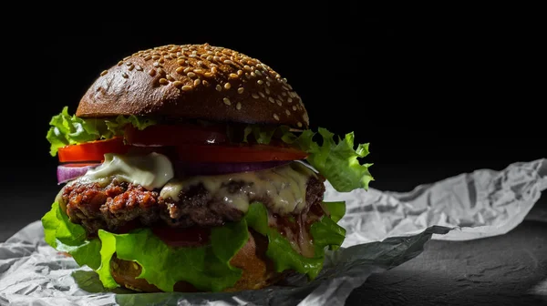 burger with meat, cheese and vegetables on dark black background