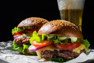 koyu siyah arka plan üzerinde et, peynir ve sebze ve bira ile iki burger