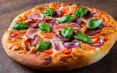 Pizza Mozzarella peynir, jambon, domates sosu, salam, soğan, biber, Baharat ve Taze fesleğen ile. Ahşap masa arka planda İtalyan pizza