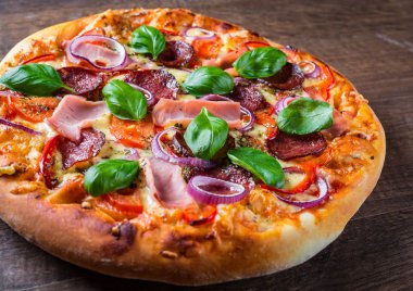 Pizza Mozzarella peynir, jambon, domates sosu, salam, soğan, biber, Baharat ve Taze fesleğen ile. Ahşap masa arka planda İtalyan pizza