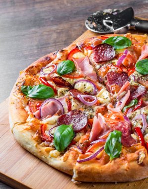 Pizza Mozzarella peynir, jambon, domates sosu, salam, soğan, biber, Baharat ve Taze fesleğen ile. Ahşap masa arka planda İtalyan pizza