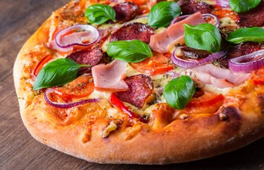 Pizza Mozzarella peynir, jambon, domates sosu, salam, soğan, biber, Baharat ve Taze fesleğen ile. Ahşap masa arka planda İtalyan pizza