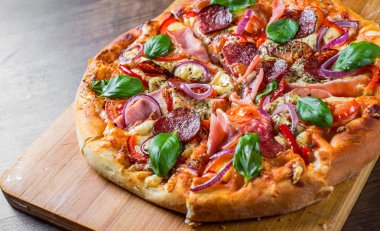 Pizza Mozzarella peynir, jambon, domates sosu, salam, soğan, biber, Baharat ve Taze fesleğen ile. Ahşap masa arka planda İtalyan pizza