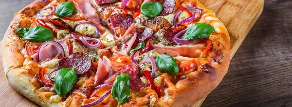 Pizza Mozzarella peynir, jambon, domates sosu, salam, soğan, biber, Baharat ve Taze fesleğen ile. Ahşap masa arka planda İtalyan pizza