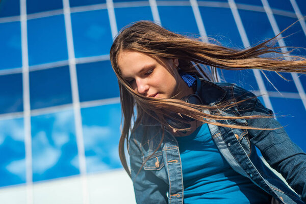 Outdoor portrait of young teenager brunette girl with long hair. Glass building on background