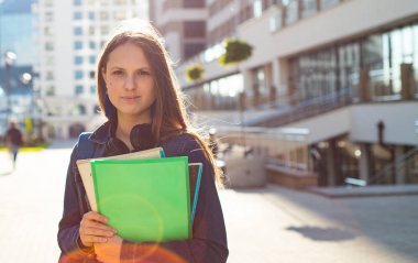 Elinde kitap tutan ve sırt çantası takan liseli kız öğrencilere. Uzun saçlı esmer bir kızın açık hava portresi. Şehirdeki kız