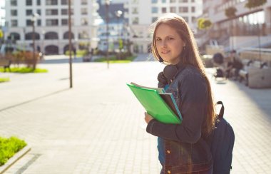 Elinde kitap tutan ve sırt çantası takan liseli kız öğrencilere. Uzun saçlı esmer bir kızın açık hava portresi. Şehirdeki kız