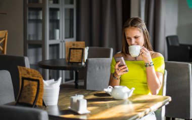 uzun saçlı Genç ergen esmer kız portre kentsel kafede kapalı oturma ve onu Smartphone kullanmak