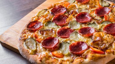 Mozzarella peyniri, salam, pastırma, Domates sosu, biber, baharat ve salatalık turşusu ile Pepperoni Pizza. Ahşap masa arka planda İtalyan pizza