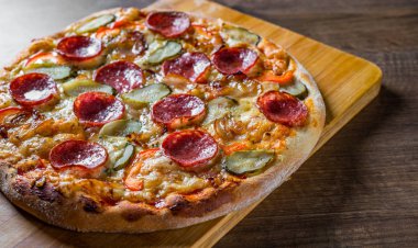 Mozzarella peyniri, salam, pastırma, Domates sosu, biber, baharat ve salatalık turşusu ile Pepperoni Pizza. Ahşap masa arka planda İtalyan pizza