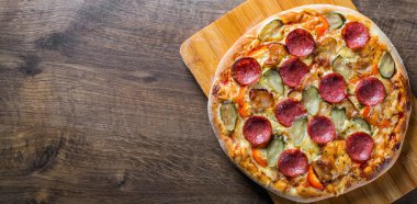 Mozzarella peyniri, salam, pastırma, Domates sosu, biber, baharat ve salatalık turşusu ile Pepperoni Pizza. Ahşap masa arka planda İtalyan pizza
