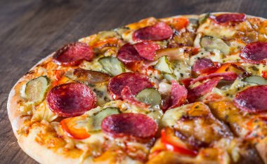 Mozzarella peyniri, salam, pastırma, Domates sosu, biber, baharat ve salatalık turşusu ile Pepperoni Pizza. Ahşap masa arka planda İtalyan pizza