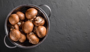 Taze çiğ mantar şampiyonları paslanmaz çelik kevgir ile koyu gri arka planda fotokopi alanı ile. en üstteki görünüm