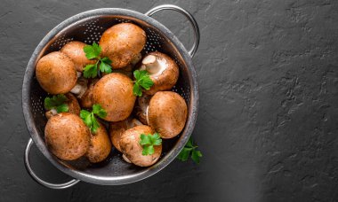 Taze çiğ mantar şampiyonları paslanmaz çelik kevgir ile koyu gri arka planda fotokopi alanı ile. en üstteki görünüm