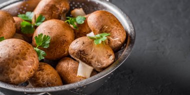 Taze çiğ mantar şampiyonları paslanmaz çelik kevgir ile koyu gri arka planda fotokopi alanı ile. en üstteki görünüm
