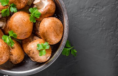 Taze çiğ mantar şampiyonları paslanmaz çelik kevgir ile koyu gri arka planda fotokopi alanı ile. en üstteki görünüm
