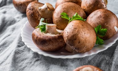 Beyaz plaka üzerinde bütün çiğ taze kahverengi mantar portobello Grubu.