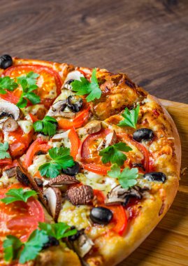 Mozzarella peyniri, Domates, biber, zeytin, mantar, Baharat ve Taze yaprak ile dilimlenmiş Pizza. Ahşap masa arka planda İtalyan pizza