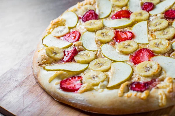 sweet Pizza with Mozzarella cheese, apple, banana, strawberries. Fruit dessert pizza on wooden table background