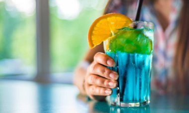 meyve ile mavi bir limonata kokteyli ile bir cam tutan genç kız eli