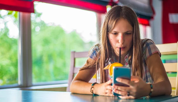 都会のカフェで屋内に座って長い髪を持つ若いティーンエイジャーブルネットの女の子の肖像画は 青いレモネードカクテルを飲み 彼女のスマートフォンを使用します — ストック写真