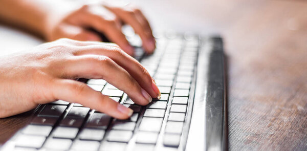 Woman working at home office hand on keyboard close up on wooden table background