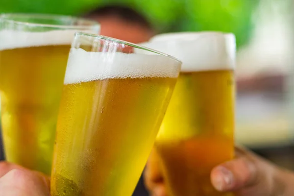 Close-up view of a three glass of beer in hand. Beer glasses clinking at outdoor bar or pub