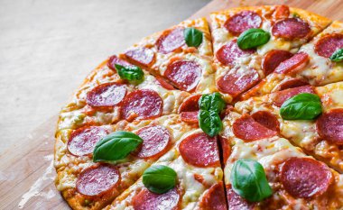 Mozzarella peynirli biberli pizza, salam, domates sosu, biber, baharat ve taze fesleğen. İtalyan pizzası ahşap masa arkasında