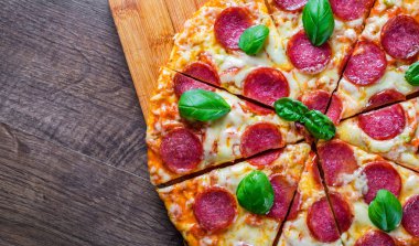 Mozzarella peynirli biberli pizza, salam, domates sosu, biber, baharat ve taze fesleğen. İtalyan pizzası ahşap masa arkasında