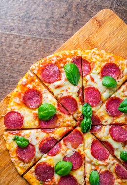 Mozzarella peynirli biberli pizza, salam, domates sosu, biber, baharat ve taze fesleğen. İtalyan pizzası ahşap masa arkasında