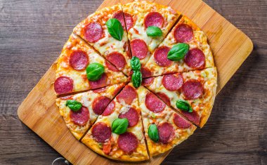 Mozzarella peynirli biberli pizza, salam, domates sosu, biber, baharat ve taze fesleğen. İtalyan pizzası ahşap masa arkasında