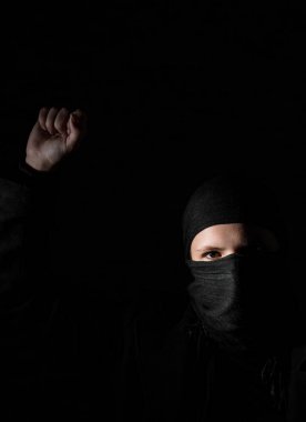 Gizli yüz protestoları ile siyah giysiler içinde genç yetişkin kız kopya alanı ile siyah arka plan üzerinde yumruk yükselterek.