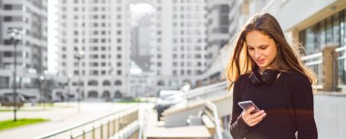 Uzun saçlı genç genç esmer kız Açık portre. güneşli bir günde sokakta akıllı telefon bakarak siyah elbiseli şehirde kız