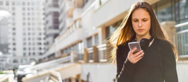 Uzun saçlı genç genç esmer kız Açık portre. güneşli bir günde sokakta akıllı telefon bakarak siyah elbiseli şehirde kız