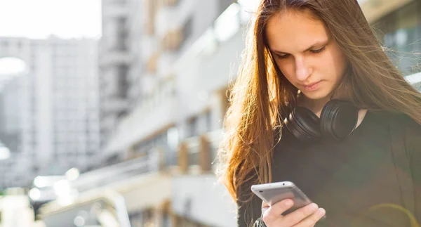 長い髪を持つ若いティーンエイジャーブルネットの女の子の屋外の肖像画 晴れた日に通りでスマートフォンを見て黒いドレスの街の女の子 — ストック写真