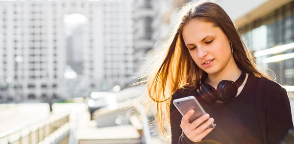 長い髪を持つ若いティーンエイジャーブルネットの女の子の屋外の肖像画 晴れた日に通りでスマートフォンを見て黒いドレスの街の女の子 — ストック写真