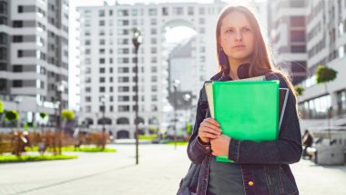 Elinde kitap tutan ve sırt çantası takan liseli kız öğrencilere. Uzun saçlı esmer bir kızın açık hava portresi. Şehirdeki kız