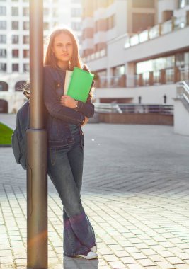 Elinde kitap tutan ve sırt çantası takan liseli kız öğrencilere. Uzun saçlı esmer bir kızın açık hava portresi. Şehirdeki kız