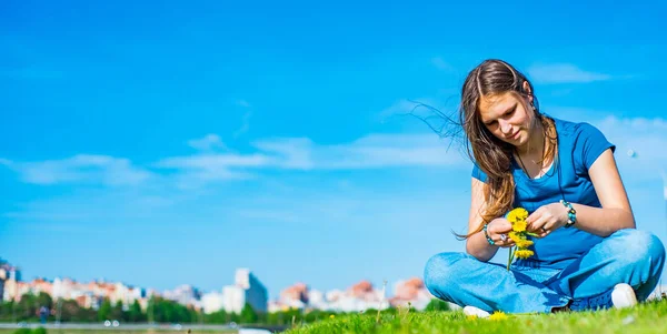長い髪を持つ若いティーンエイジャーブルネットの女の子は草の上に座って コピースペースと空の背景に黄色のタンポポの花の花輪をリース — ストック写真