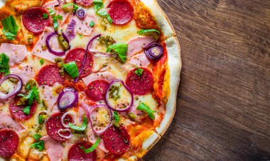 Pizza Mozzarella peynir, jambon, domates sosu, salam, soğan, biber, Baharat ve Taze fesleğen ile. Ahşap masa arka planda İtalyan pizza