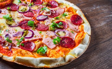 Pizza Mozzarella peynir, jambon, domates sosu, salam, soğan, biber, Baharat ve Taze fesleğen ile. Ahşap masa arka planda İtalyan pizza