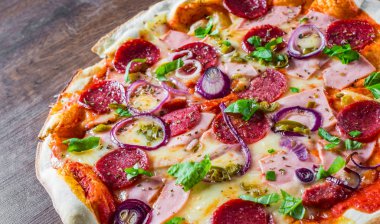 Pizza Mozzarella peynir, jambon, domates sosu, salam, soğan, biber, Baharat ve Taze fesleğen ile. Ahşap masa arka planda İtalyan pizza