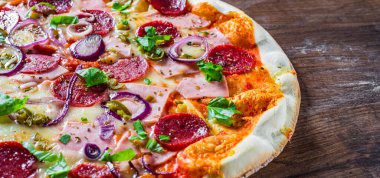 Pizza Mozzarella peynir, jambon, domates sosu, salam, soğan, biber, Baharat ve Taze fesleğen ile. Ahşap masa arka planda İtalyan pizza